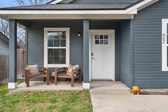 entrance to property featuring fence, covered porch, and a shingled roof