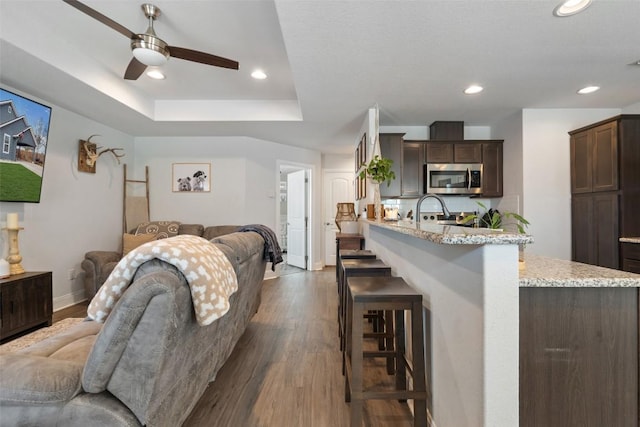 interior space with a tray ceiling, dark wood finished floors, recessed lighting, baseboards, and ceiling fan