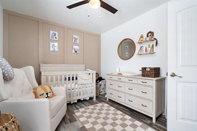 bedroom with ceiling fan, a nursery area, and wood finished floors