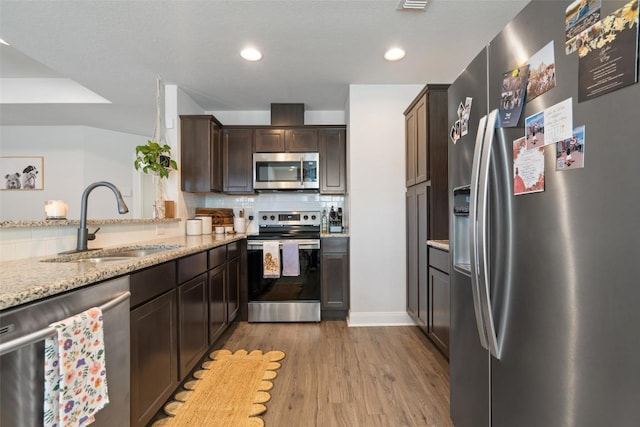 kitchen featuring wood finished floors, a sink, decorative backsplash, dark brown cabinets, and appliances with stainless steel finishes