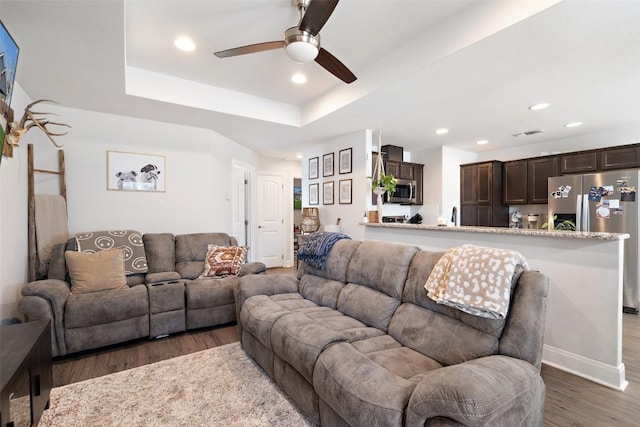 living room featuring wood finished floors, visible vents, baseboards, recessed lighting, and a raised ceiling