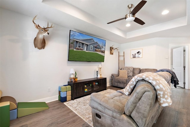 living area featuring a raised ceiling, a ceiling fan, wood finished floors, recessed lighting, and baseboards