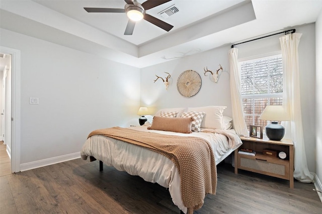 bedroom with visible vents, a raised ceiling, baseboards, and wood finished floors