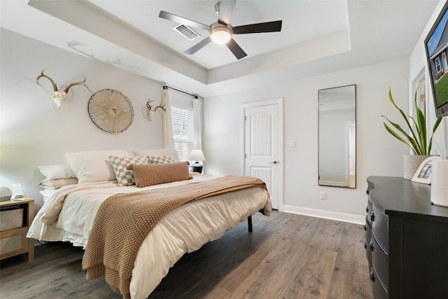 bedroom featuring a tray ceiling, baseboards, visible vents, and wood finished floors