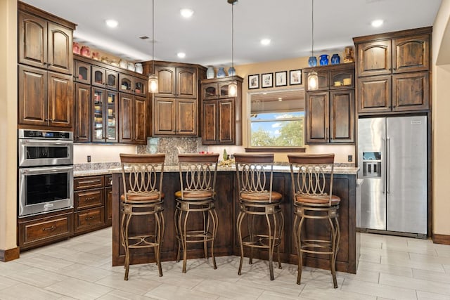 kitchen with dark brown cabinets, a center island, glass insert cabinets, hanging light fixtures, and stainless steel appliances