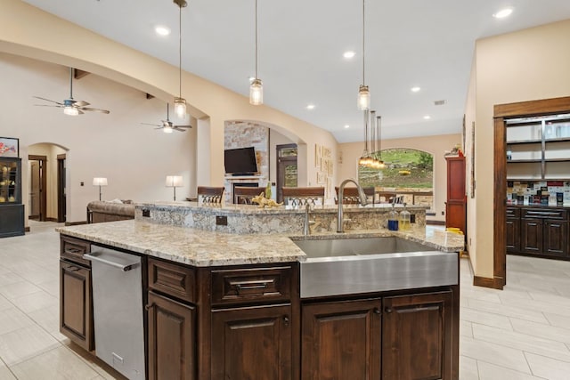 kitchen with arched walkways, open floor plan, dark brown cabinetry, and a sink