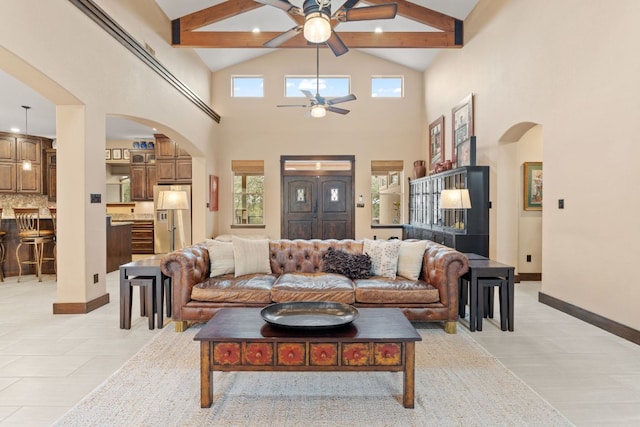 living area with beam ceiling, a ceiling fan, arched walkways, and baseboards