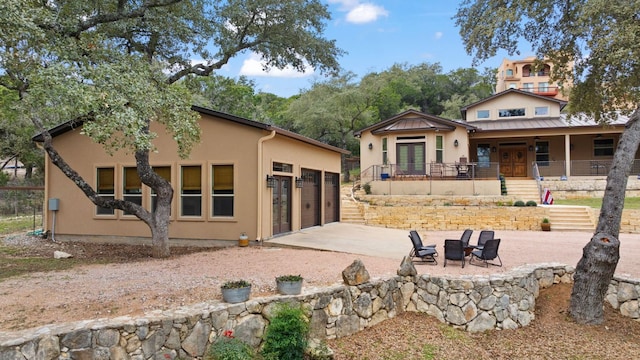 rear view of house featuring driveway, a standing seam roof, stucco siding, french doors, and metal roof