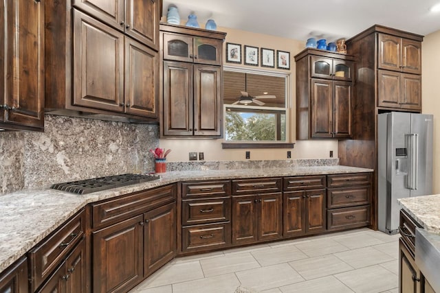 kitchen featuring light stone counters, dark brown cabinets, glass insert cabinets, appliances with stainless steel finishes, and backsplash