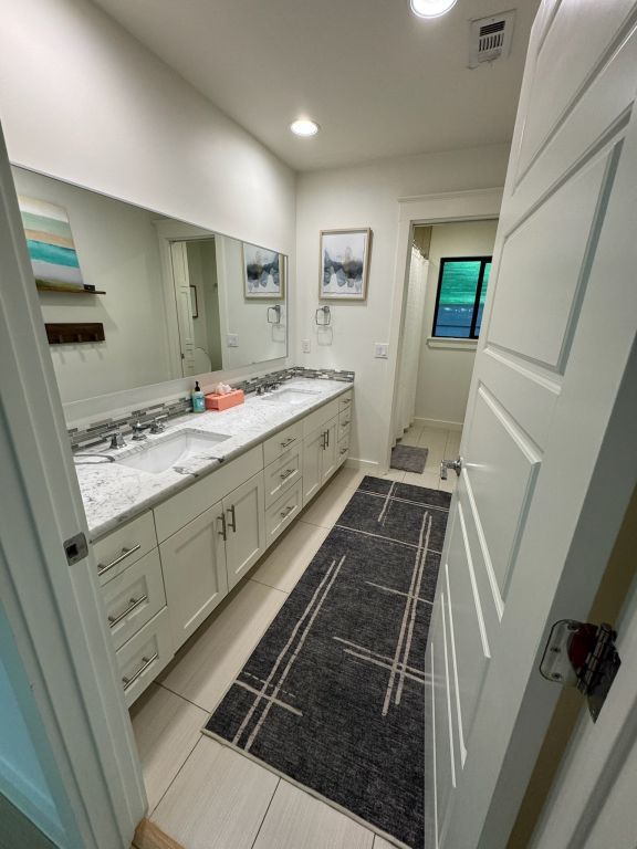 bathroom featuring tile patterned flooring, visible vents, curtained shower, double vanity, and a sink