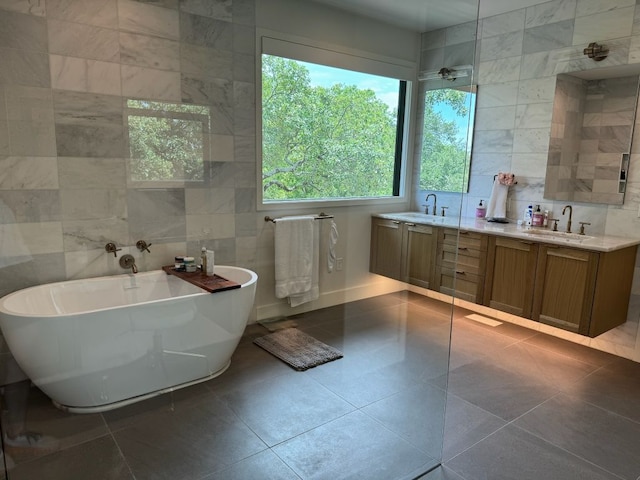 bathroom featuring tile walls, a freestanding tub, double vanity, and a sink