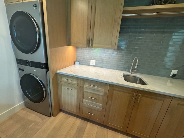 laundry area featuring a sink, light wood-style flooring, and stacked washing maching and dryer