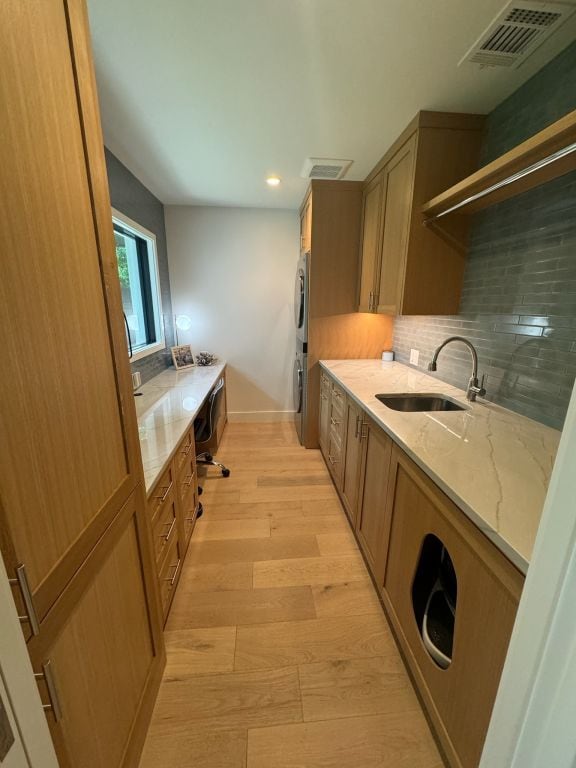 kitchen featuring light wood finished floors, backsplash, light stone counters, stacked washer and clothes dryer, and a sink