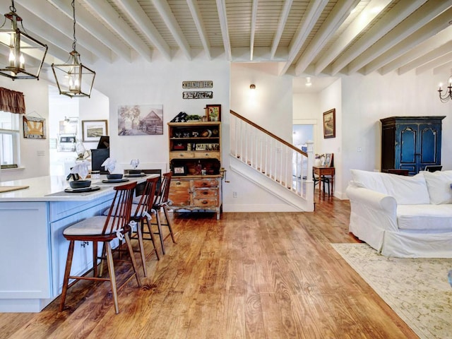 kitchen with a chandelier, light countertops, a kitchen bar, beam ceiling, and light wood-style floors