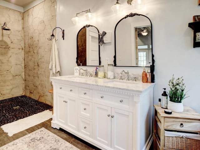 full bath featuring double vanity, tiled shower, and a sink