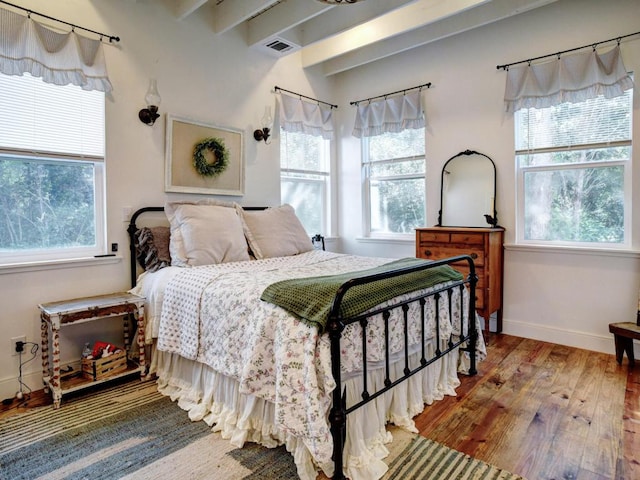 bedroom with beam ceiling, visible vents, baseboards, and wood finished floors