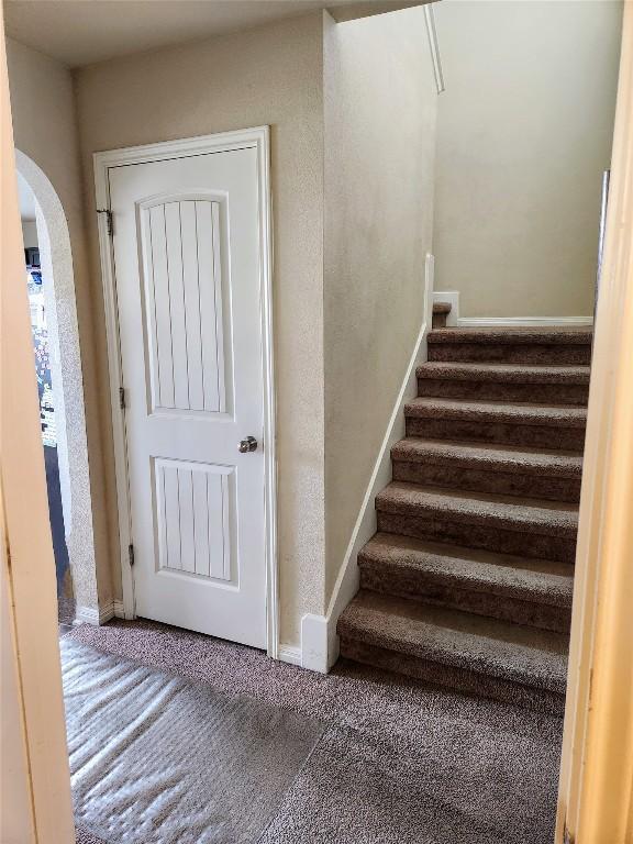 staircase with arched walkways, carpet flooring, and baseboards