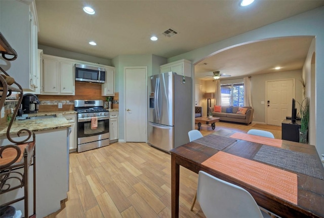 kitchen featuring arched walkways, white cabinetry, stainless steel appliances, and a sink