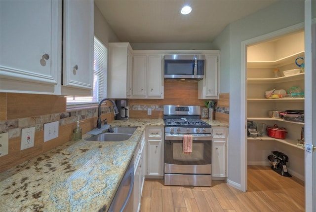 kitchen featuring backsplash, stainless steel appliances, light wood-style floors, white cabinetry, and a sink