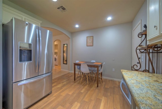 kitchen featuring visible vents, washer / clothes dryer, arched walkways, light wood-style floors, and appliances with stainless steel finishes