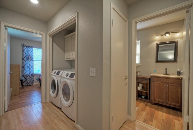 laundry room with a sink, cabinet space, independent washer and dryer, and light wood-style flooring