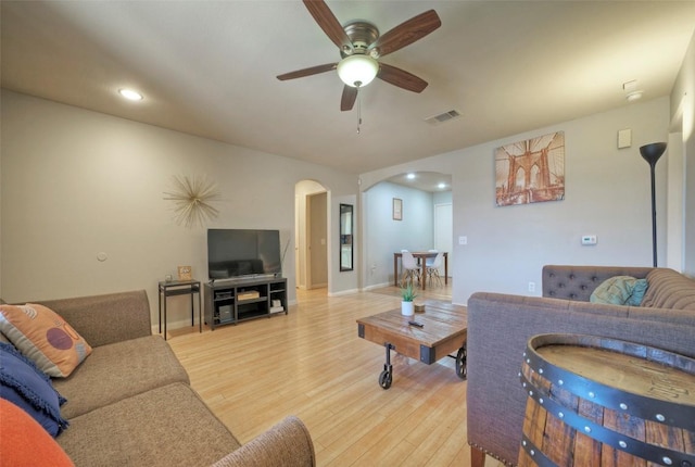 living area with baseboards, visible vents, light wood-style flooring, arched walkways, and ceiling fan