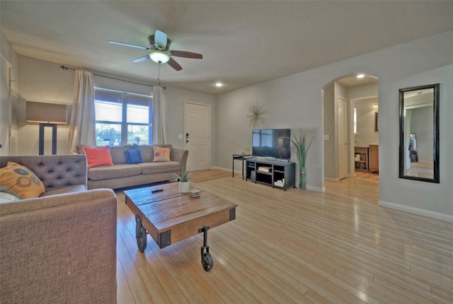 living area featuring arched walkways, light wood finished floors, a ceiling fan, and baseboards