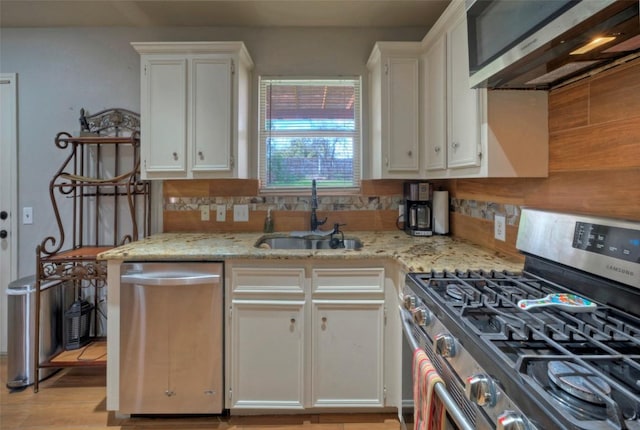 kitchen featuring a sink, light stone counters, ventilation hood, stainless steel appliances, and white cabinets