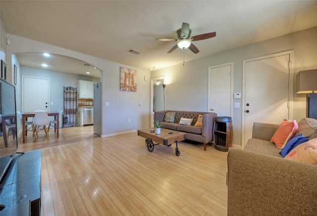 living area featuring visible vents, a ceiling fan, arched walkways, light wood-style floors, and baseboards