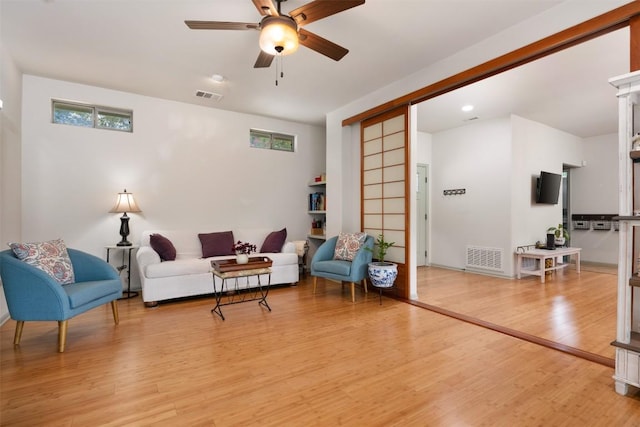 living room with light wood finished floors, visible vents, and a ceiling fan