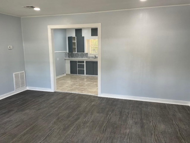 spare room featuring visible vents, baseboards, dark wood-style flooring, and crown molding