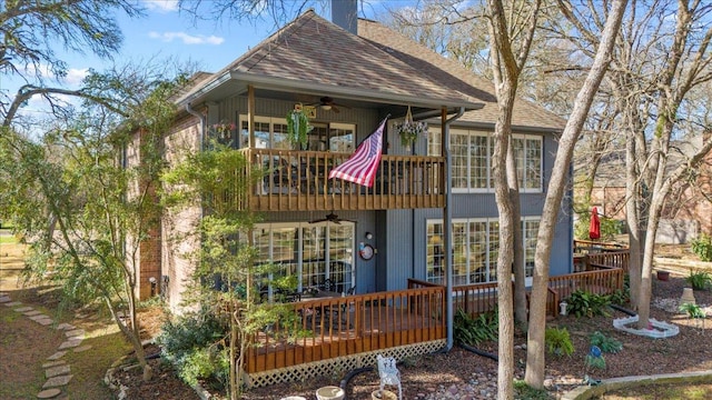 back of house featuring a balcony, a ceiling fan, a shingled roof, a chimney, and a deck