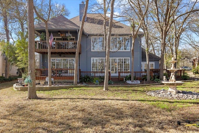 back of house featuring ceiling fan, roof with shingles, a chimney, a yard, and a balcony