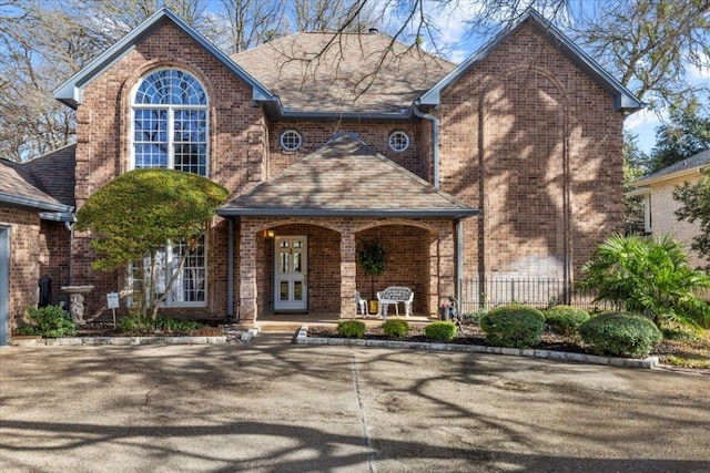 view of front of house with french doors, brick siding, a porch, and roof with shingles