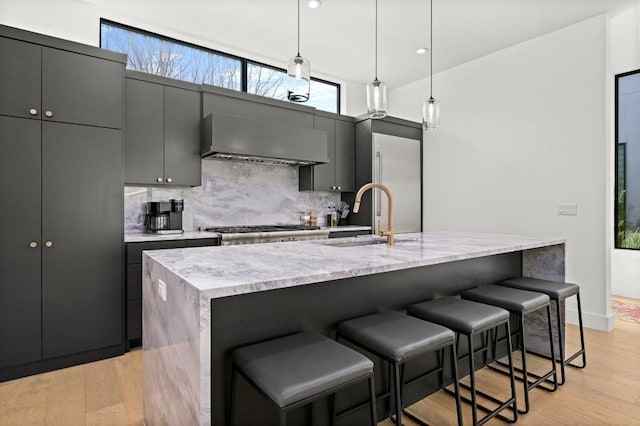 kitchen featuring a sink, decorative backsplash, light wood-style floors, and wall chimney exhaust hood