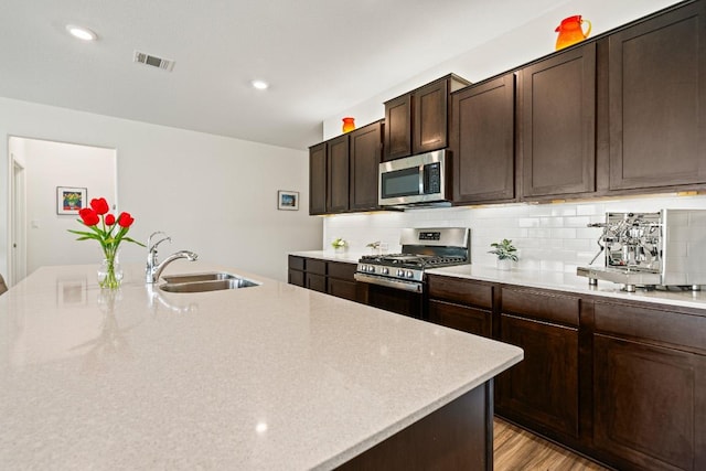 kitchen featuring visible vents, dark brown cabinetry, decorative backsplash, appliances with stainless steel finishes, and a sink