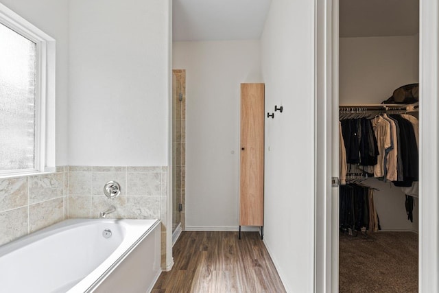 bathroom featuring a shower stall, a walk in closet, baseboards, wood finished floors, and a bath