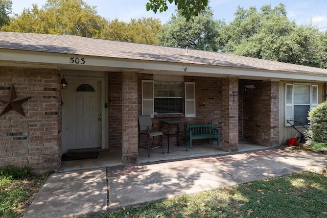 property entrance featuring a porch, brick siding, and roof with shingles