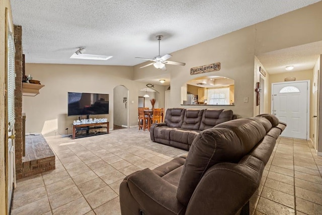 living area with a ceiling fan, light tile patterned flooring, arched walkways, vaulted ceiling, and a textured ceiling