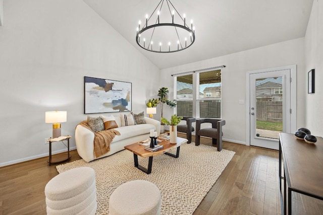 living room with a notable chandelier, wood finished floors, baseboards, and high vaulted ceiling