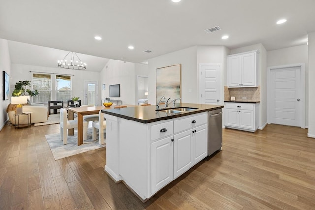 kitchen featuring visible vents, light wood finished floors, a sink, dark countertops, and open floor plan