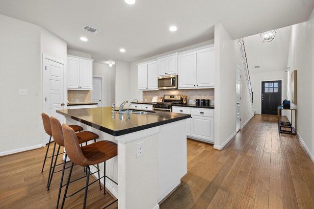 kitchen featuring dark countertops, visible vents, appliances with stainless steel finishes, light wood-style floors, and a sink