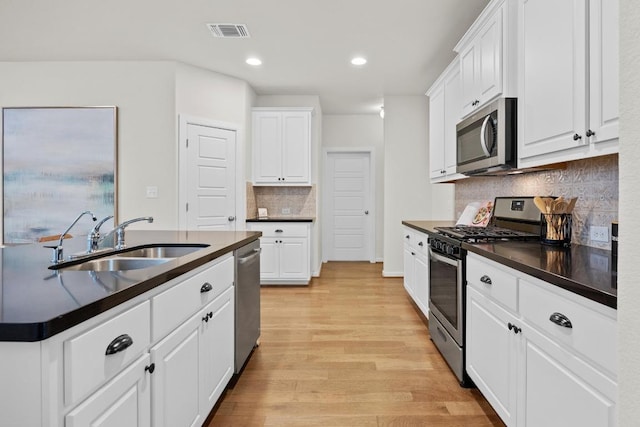 kitchen with a sink, stainless steel appliances, dark countertops, and visible vents