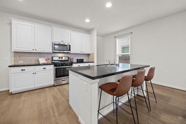 kitchen featuring decorative backsplash, dark countertops, an island with sink, and appliances with stainless steel finishes