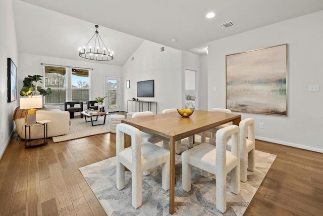 dining space with visible vents, baseboards, lofted ceiling, wood finished floors, and a notable chandelier