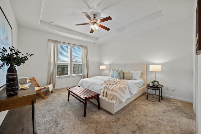 carpeted bedroom with a tray ceiling, baseboards, and ceiling fan