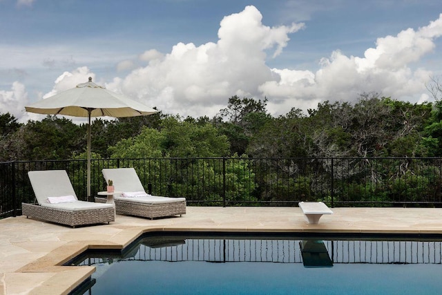 view of swimming pool with a fenced in pool, a wooded view, a patio, and a diving board