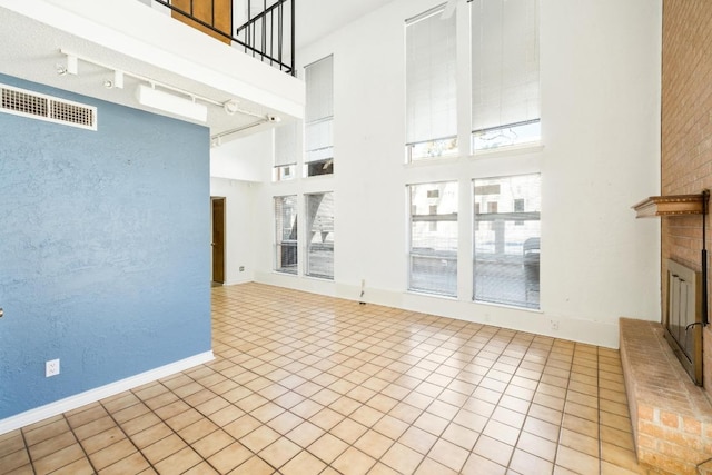 121 Scott St, San Marcos, TX 78666 - unfurnished living room with visible vents, track lighting, a high ceiling, light tile patterned flooring, and a brick fireplace