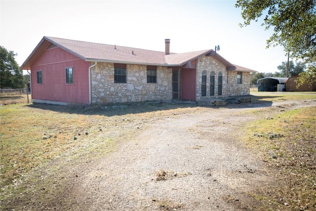 view of front facade featuring stone siding, driveway, and fence