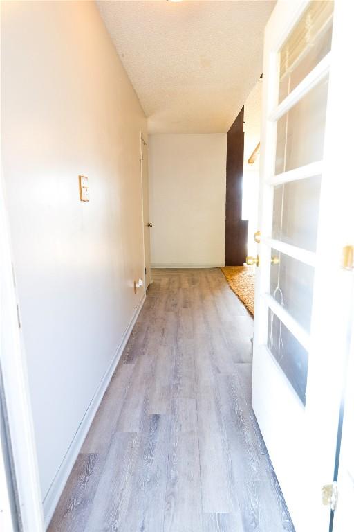 corridor featuring baseboards, a textured ceiling, and wood finished floors